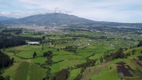 Cinematic drone clip moving over the green fields towards a small town under a mountain in Puichig, Equador