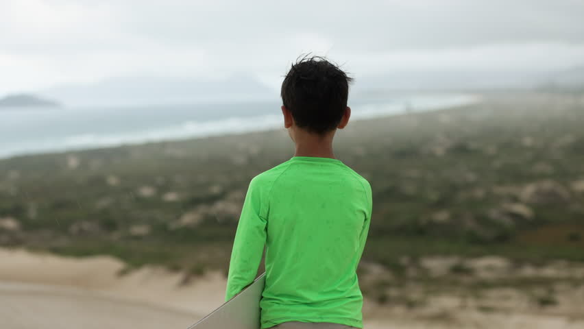 Boy sand boarding on dune hills next to ocean turns and prepares to try - hand held action shot