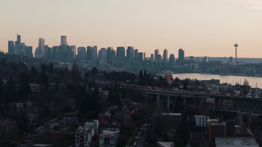 Traffic flows across a bridge in the evening golden hour with the downtown Seattle skyline and Space Needle by Lake Union in the background