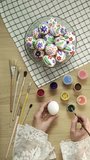 Process of making handmade painted Easter eggs. Close-up of hands painting Easter egg with paint and brush. Preparing for Easter, Christian tradition Vertical video