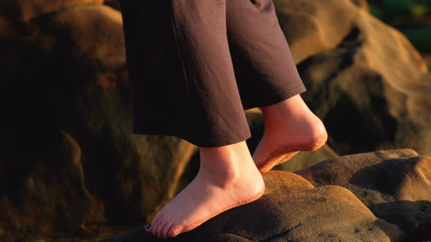 a slow-motion video depicting a teenage girls feet with painted toenails, her dog, balancing on rocks by the tidepool on a pacific coast beach in california