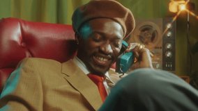 Joyful African-American man in retro outfit sitting on chair, smiling and having conversation on a landline phone in studio with vintage interior. Zoom Shot - Powered by Shutterstock - Get 15% off with code: PIKWIZARD15