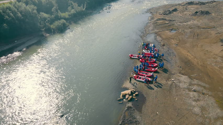 Aerial View of Rafting Preparation on River Shore, Group of rafters preparing their boats for an adventurous trip on a riverbank.