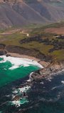 Craggy shore of the Pacific Ocean at Morro Bay, California, USA. Bare brown mountains at backdrop. Aerial perspective. Vertical video.
