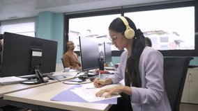 Happy businesswoman looking away while writing on documents at desk in creative office