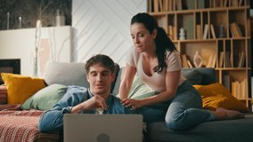 Married couple using laptop sitting on sofa living room. Happy young spouses enjoy online shopping planning vacation at home weekend evening. Modern family using gadgets for comfortable lifestyle. - Powered by Shutterstock - Get 15% off with code: PIKWIZARD15