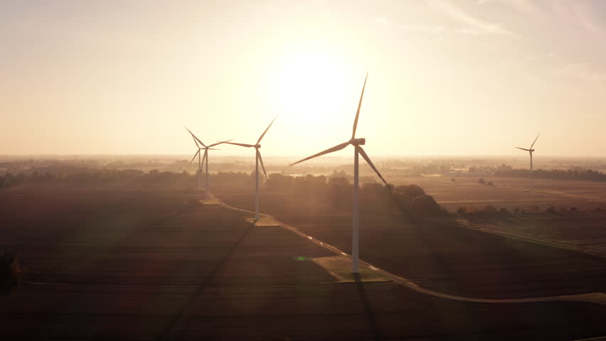 Aerial view of a rotating wind turbine blade at a wind farm in a field against the low sun. Green and renewable energy concept. Wind turbines produce clean, renewable energy for sustainable 