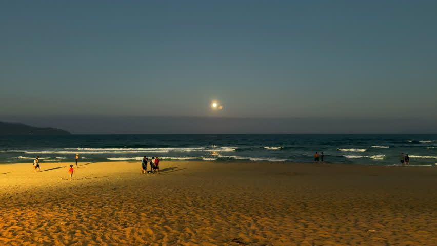 Full moon rising over a beach. Moonrise on a calm beach. People on a beach while the moon rises. Da Nang, Vietnam.