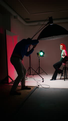 Photographer capturing a red-haired model in a studio setting, colored lighting and professional equipment in use. Behind the scenes of fashion photography. Design for educational content, photography