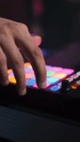 A DJ's fingers press the buttons of an audio controller at a party in a nightclub. Close-up, vertical video.