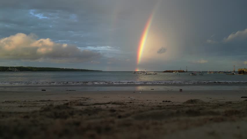 A bright rainbow over the ocean on the horizon, even two parallel rainbows at dawn over the sea on the horizon, a bright multi-colored rainbow located on the horizon at dawn on the beach.