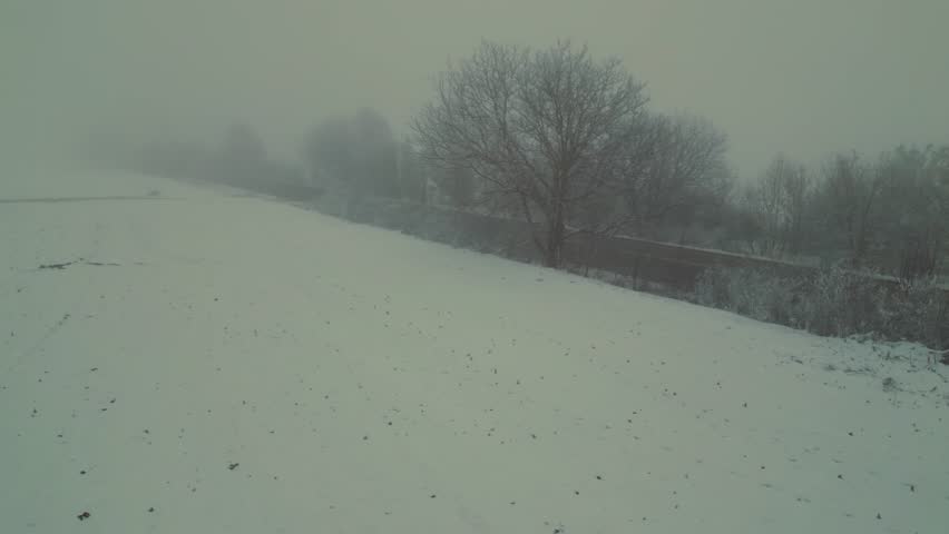 Drone footage flying through thick fog. Shots of rolling fog and clouds with darkened sun through and above. Misty winter frozen farmland and woods filmed from above.