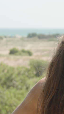 The young woman blows her long hair in the wind. She looks at the sea in the distance. Vertical. Social Media
