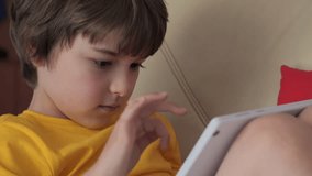 Portrait of Cute Boy Playing Game on Tablet PC Relaxing in Living Room. Child Browsing Social Media. Child Using Tablet PC Sitting on Sofa at Home, Homeschooling, Distant Remote Education.