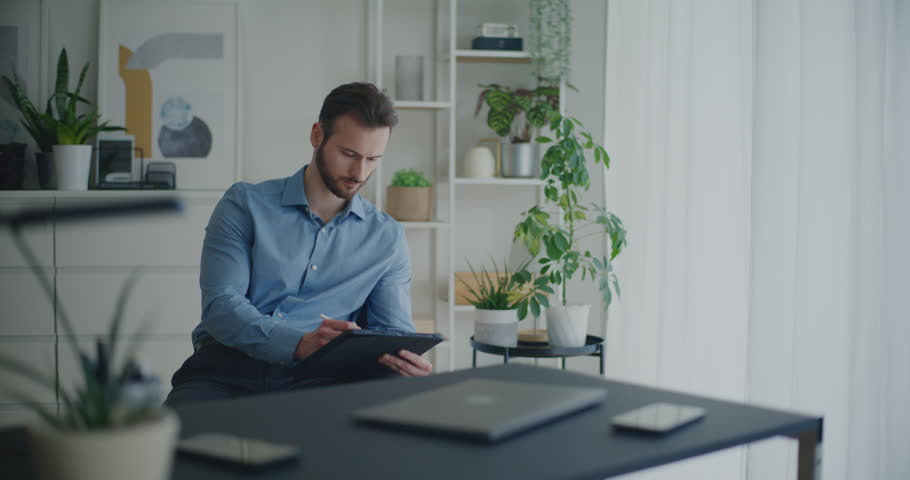Confident young male professional writing strategy on digital tablet with stylus while sitting near desk at corporate workspace Royalty-Free Stock Footage #3458847011