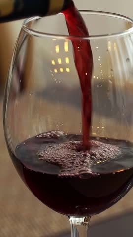 Close up of hand pours dry red wine from bottle into glass in restaurant. French wine. Drink. Vertical shot