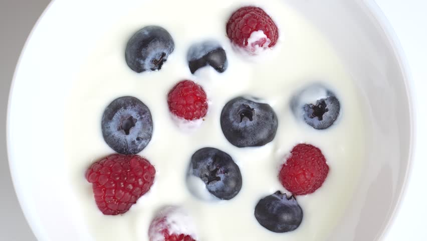 Greek yogurt with raspberry and blueberry scooped with spoon from a bowl, close up