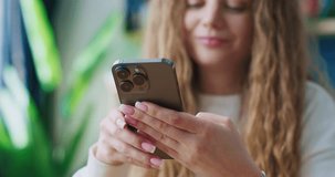 Portrait of smiling female holding smartphone. Young woman taping text message. Stylish apartment. Woman chatting by smartphone. Female using new smartphone app. Online communication.