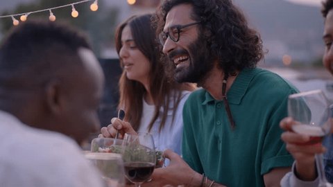 Smiling people having fun at reunion of friends BBQ food and beverage. Couple eating and drinking happiness on sunset at a terrace. Laughing group of multiracial friends celebrating a meal outdoor Video Stok