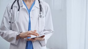 Female doctor using digital tablet in clinic. Healthcare professional with a stethoscope around her neck operating a touchscreen computer while standing on the glass background. Medicine and