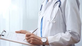 Female doctor taking notes on clipboard. Close-up of a unrecognizable female healthcare professional writing and filling um medication history records form while standing straight in clinic