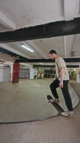 Vertical shot of young guy riding on skateboard up and down skatepark bowl during practice