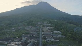 Fly over beautiful scenery of Indonesian countryside with Merapi Mountain emits smoke on the background. Stabelan Village on the slope of Merapi Volcano. 4K aerial drone shot.