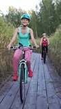 Two young women ride bicycles on a wooden ecological trail among the reeds. Vertical video