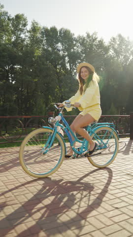 Vertical Screen: Beautiful cheerful female riding bicycle on city street and smiling on sunny day. Young woman on bike feeling happy and relaxed, weekend leisure
