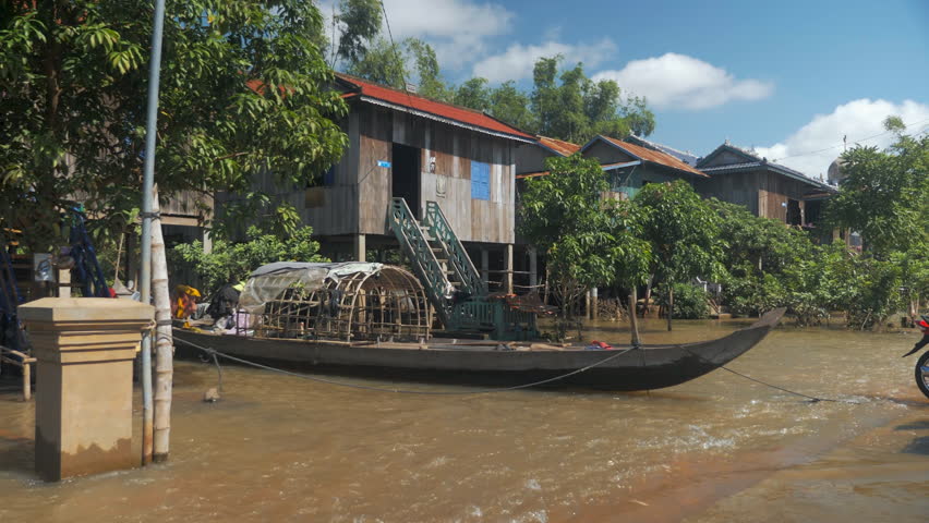 A wooden boat in the front of stilt houses encircled by floodwaters 