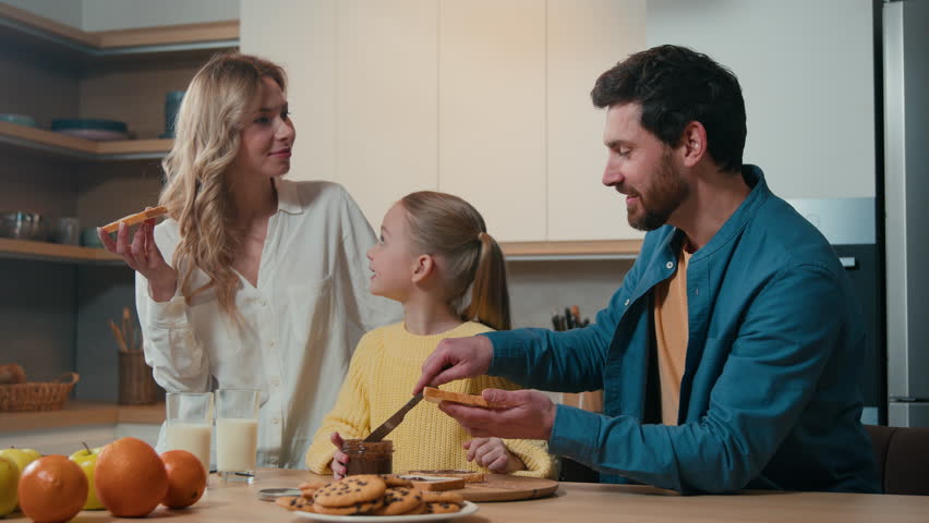 Happy smiling Caucasian family parents with child kid daughter eat prepare cook breakfast together at kitchen home enjoy organic food delivery eating chocolate sandwich mother, father little girl Royalty-Free Stock Footage #3459176699