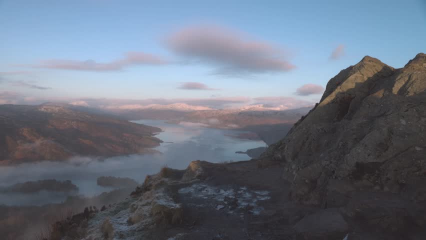 shot of a hiker walking towards the edge overlooking Loch Katrine from Ben A