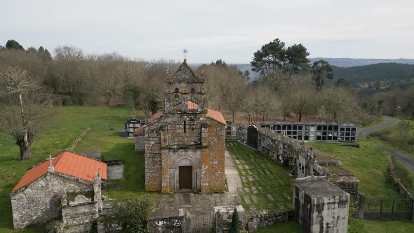 Quaint mossy weathered old chapel surrounded by cemetery urn holders of Church of Santa Maria de Vilela in Punxin Ourense Spain