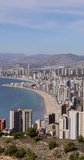 Portrait video footage of the town of Benidorm in Spain in the summer time taken from the northern hill in the summer time showing many high rise apartments and building along side the Levante Beach