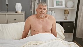 Middle-aged shirtless man sitting on bed in a modern bedroom looking away contemplatively. - Powered by Shutterstock - Get 15% off with code: PIKWIZARD15