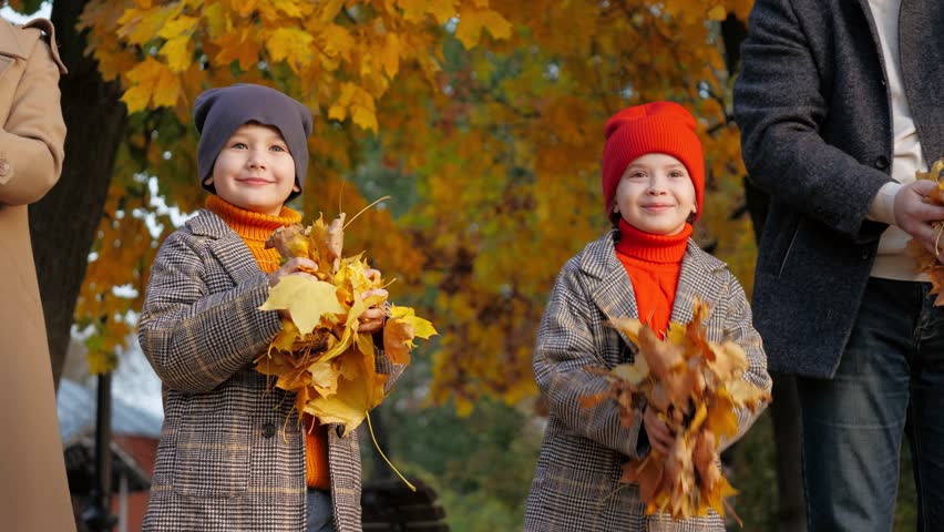 Daughter with son enjoy throwing autumn leaves up with parents. Preschooler children hold autumn leaves standing near parents. Happy boy and girl spend time together with parents among autumn leaves