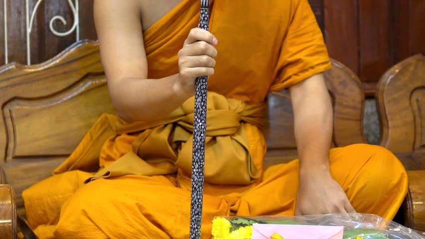 Locked shot and close up the Thai Young monk is sitting on wooden chair and hold a talipot fan in front and praying ceremony inside a temple in Bangkok, Thailand