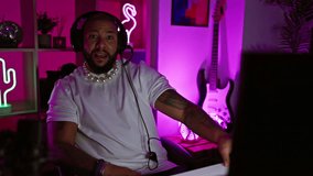 An adult black man with a beard enjoys gaming at night in a neon-lit room.