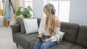 A young woman with blonde hair listens to music on headphones and uses a tablet in her modern living room - Powered by Shutterstock - Get 15% off with code: PIKWIZARD15