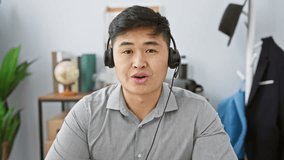 A young asian man with headphones sits at his desk in a modern office, embodying professionalism and concentration.