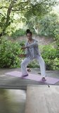 Vertical video of focused biracial woman practicing yoga on sunny terrace, slow motion. Lifestyle, wellbeing in nature, yoga, fitness, healthy lifestyle and domestic life, unaltered.