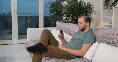 Attractive Man Watch Movie on Mobile Phone Night Entertainment Sit on Home Sofa