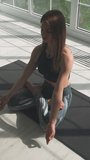 Wellness, young woman meditates and does yoga, a calm mood, relaxing in a white room filled with light, the girl is sitting on the floor, vertical video for social networks.