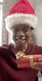Vertical video of african american man wearing santa hat having video call at home, slow motion. Lifestyle, celebration, christmas, communication and domestic life, unaltered.