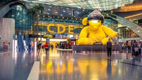 Doha, Qatar, 3 January 2018. Hamad International Airport in Doha, departure hall with a sculpture, often known as "Lamp Bear". Blurred crowd of people. Time lapse. Camera moves from left to right