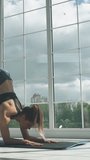 Sporty woman is doing yoga in a room filled with light, the female performs yoga handstands near the large window, vertical video for social networks.