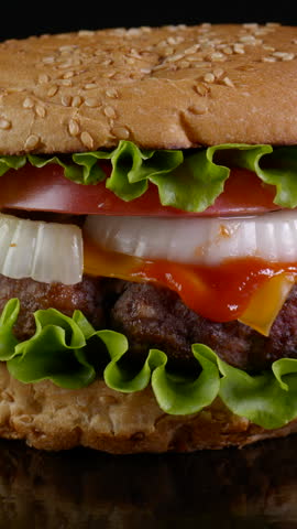 Fresh appetizing Beef Burger is rotating. Delicious burger with fresh iceberg cabbage, onions, tomatoes and grilled steak. Rotating - fast food, Close-up, vertical footage