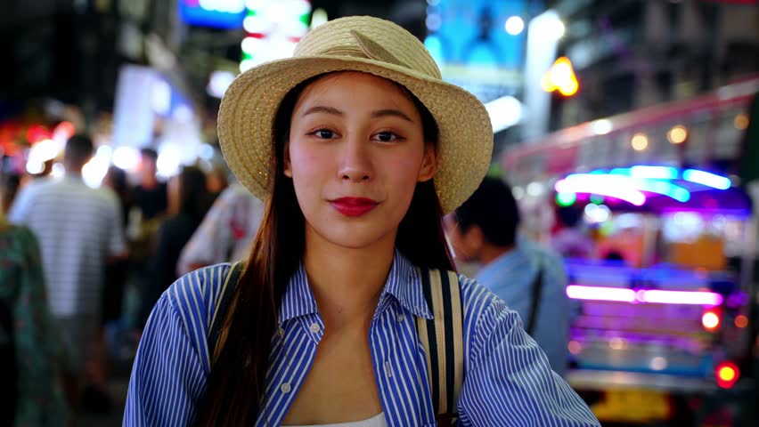 Young adult Asian woman smiles in front of camera on the street at night in Bangkok, Thailand. Solo backpacker enjoying travel vibes on street. Southeast Asia tourism concept Royalty-Free Stock Footage #3459614047
