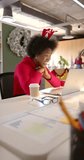 Vertical video of african american casual businesswoman making video call in office, slow motion. Casual office, business, communication, christmas, tradition, celebration and work, unaltered.