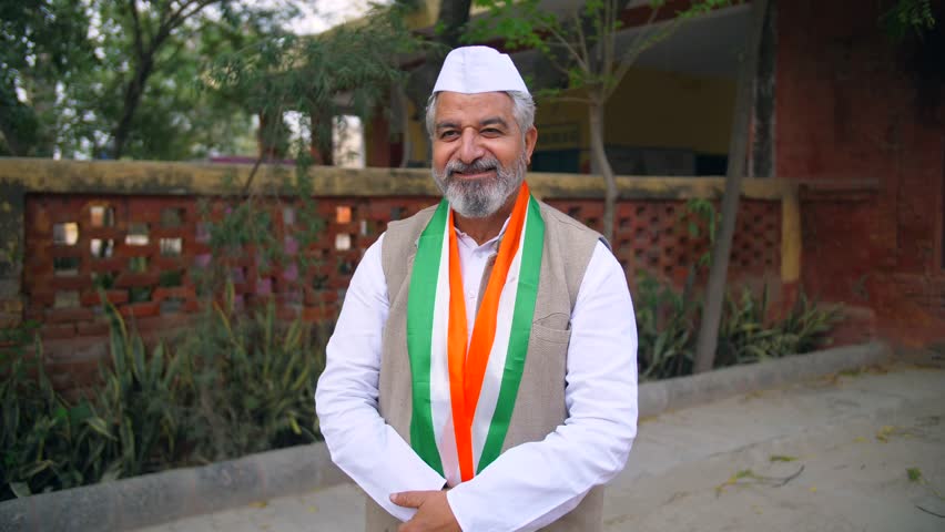 An Indian political party leader folding his hands and posing for the camera - assembly election, election winner, Indian democracy. A leader of the government party with a tricolour scarf strikes ...
